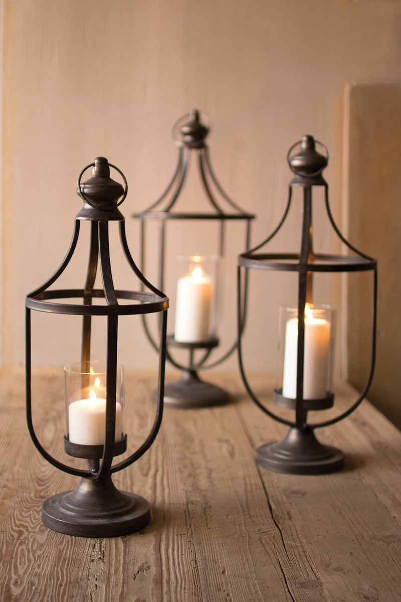set of three metal lanterns with glowing candles on a wood table